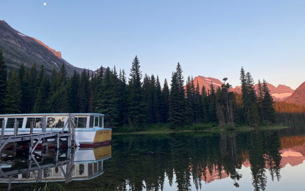 Sunrise over mountains and trees at Many Glacier Hotel on Swiftcurrent Lake with boat in dock