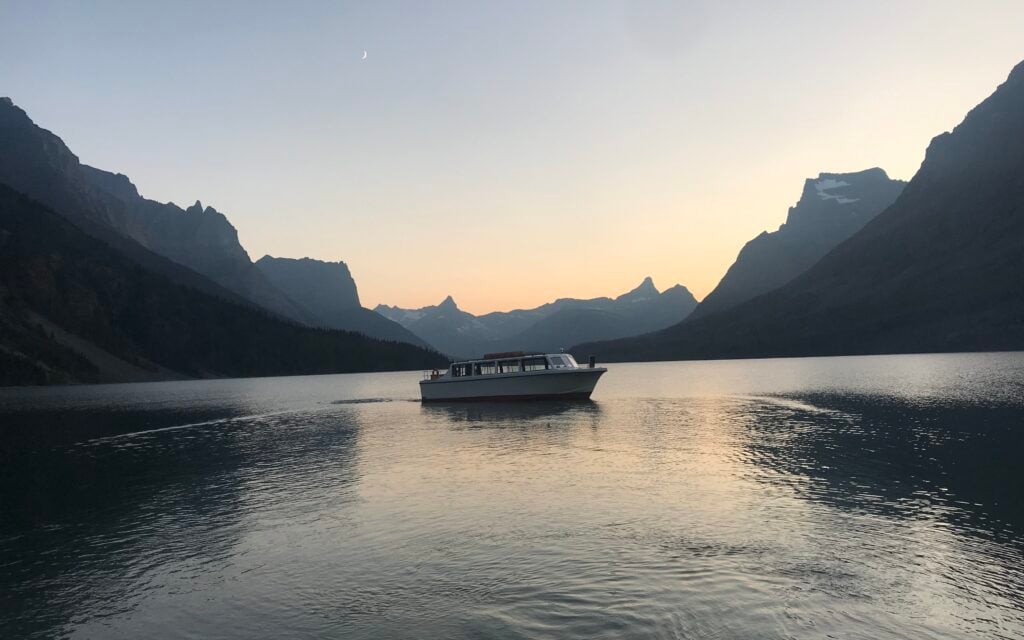 glow from sunset behind mountains and St. Mary Lake in Glacier with boat in the middle
