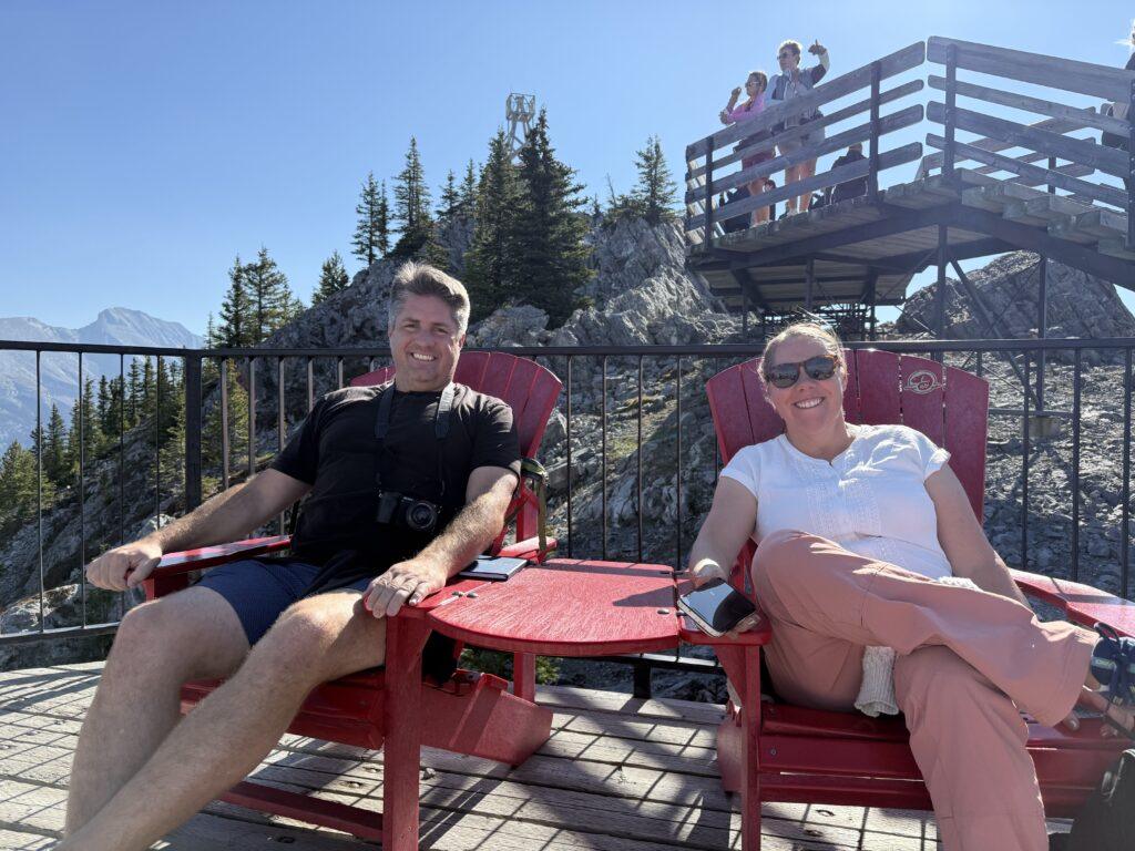 man and woman sitting on red Adirondack chairs on boardwalk