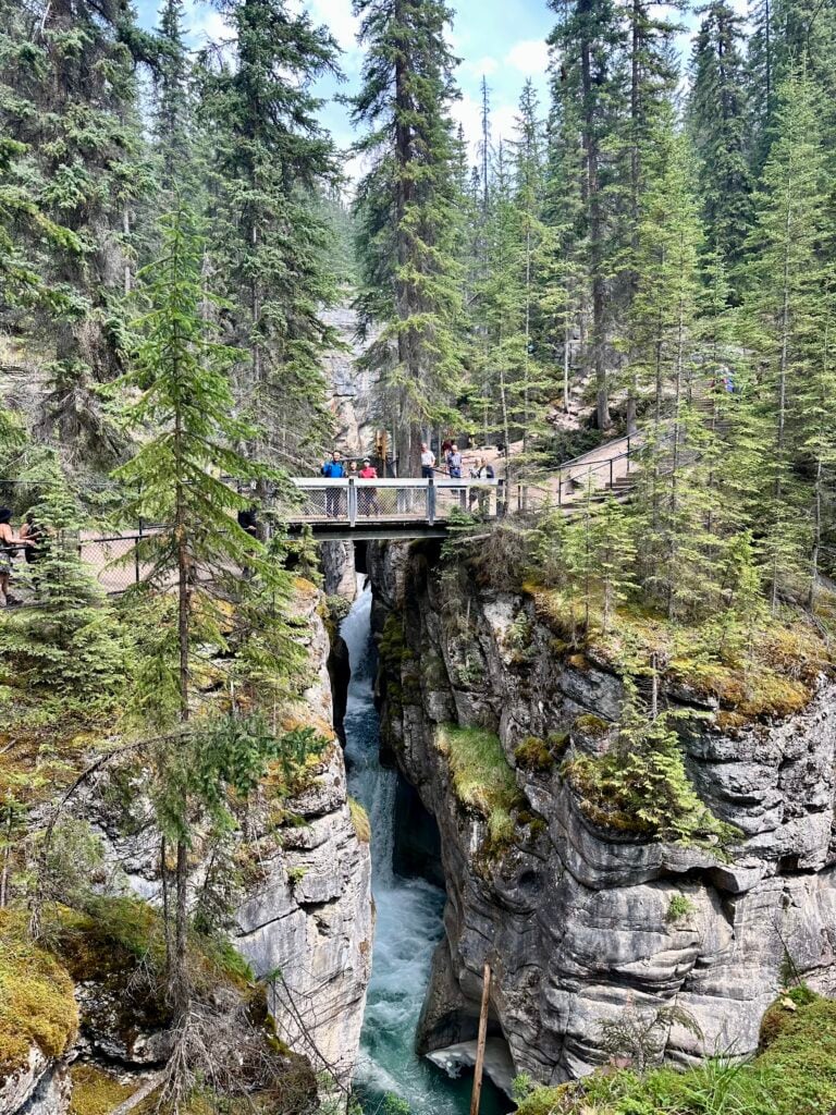 view of people standing on bridge over narrow canyon with waterfall behind