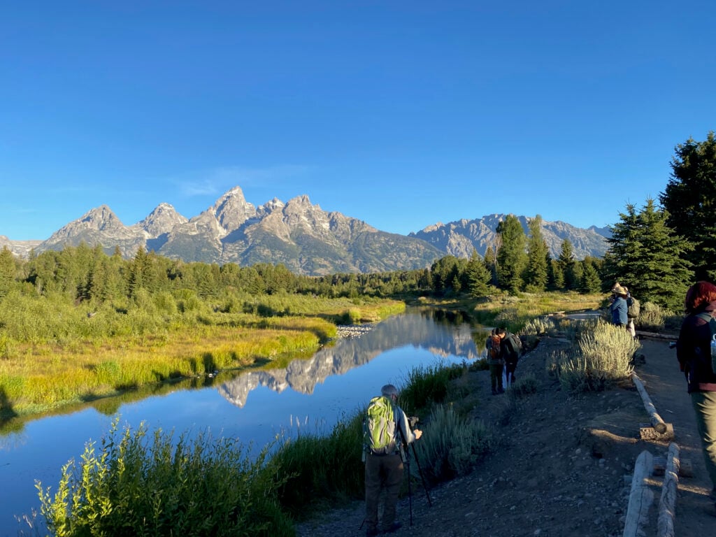 people standing on edge of river with Tetons in background