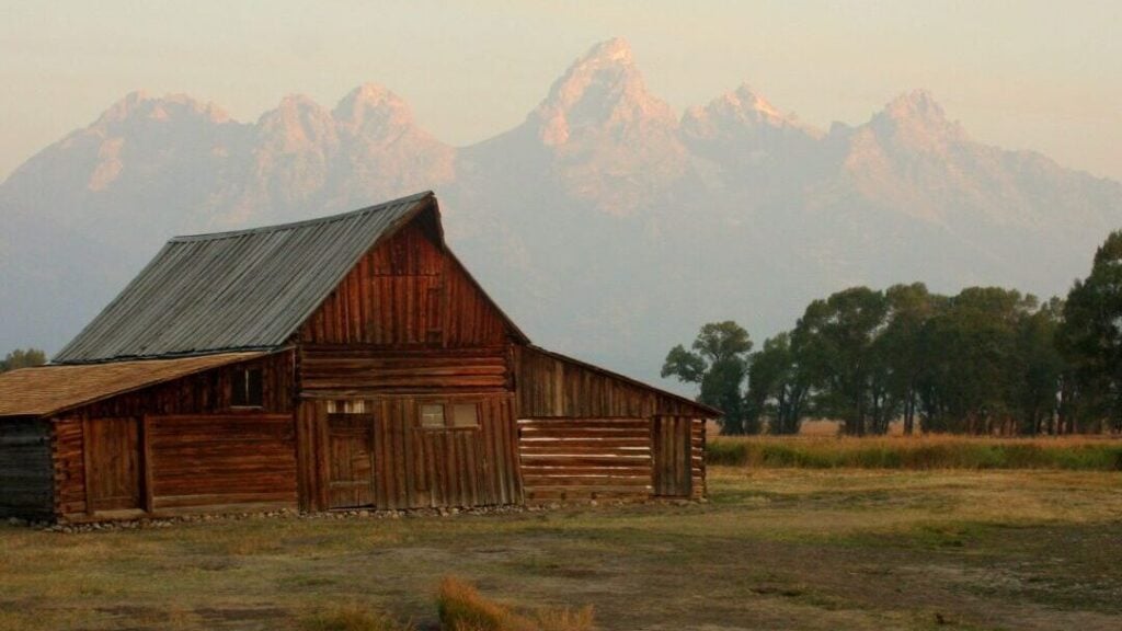 old barn in meadow with Tetons in the distance
