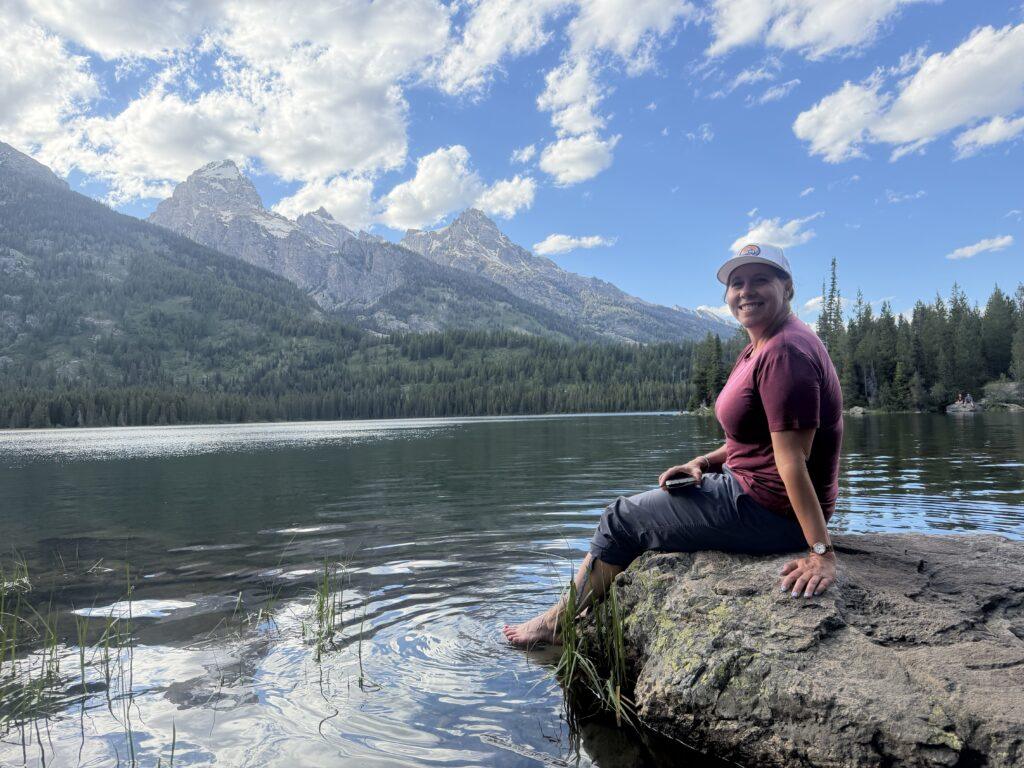 woman sitting on rock with feet in lake