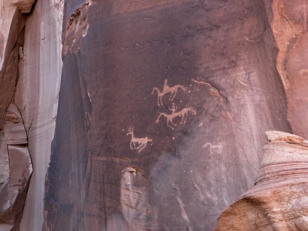 Petroglyphes on red rock showing men on horses and an elk