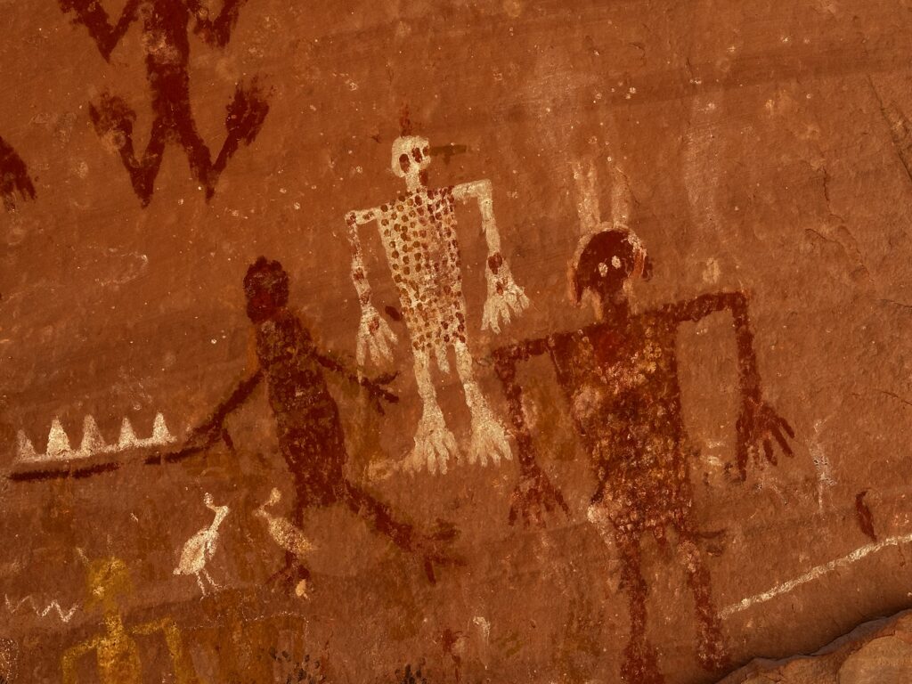 3 humanoid petroglyphs with spots on them on a red rock wall