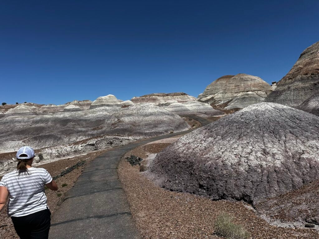 Woman walking on an asphalt trail through mound of blue and white sand