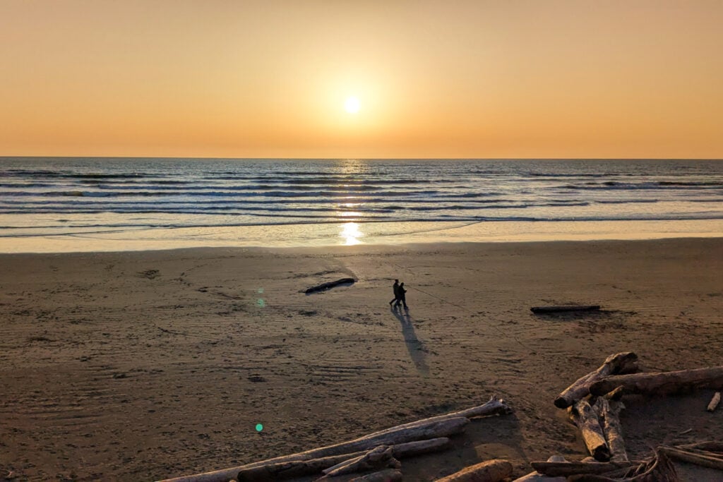 people walking along beach at sunset