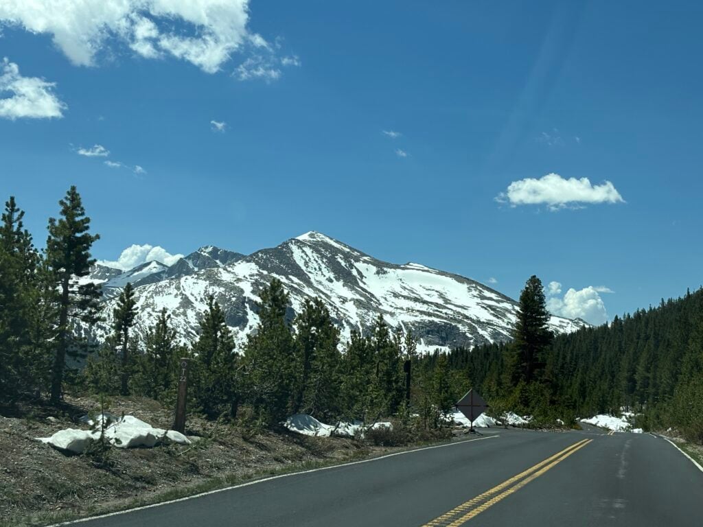 road with snow on the side of the road and snow covered mountain in the back