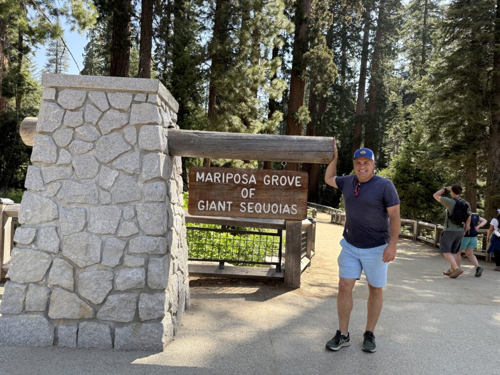 man standing in front of Mariposa Grove sign