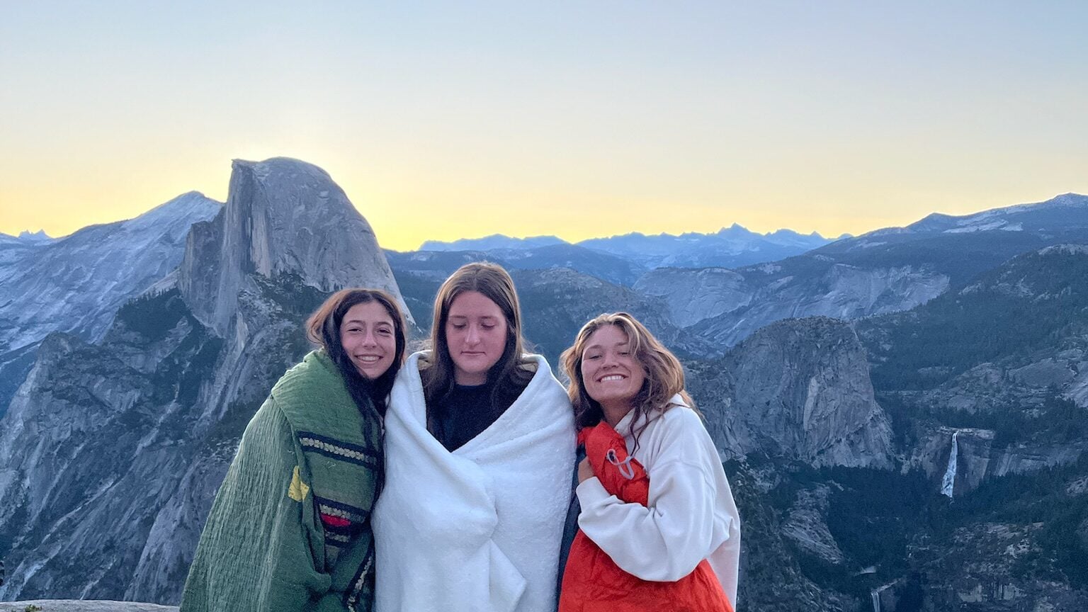 girls with blankets watching sunrise on cliff