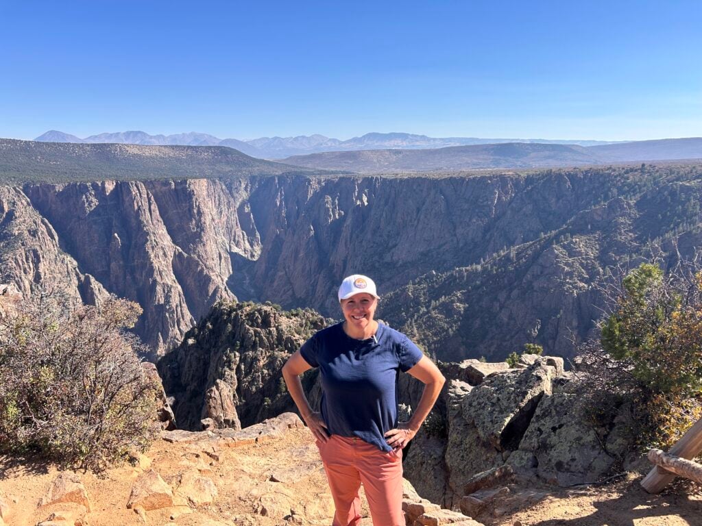 Woman in white baseball cap standing outside in front of a black canyon behind her