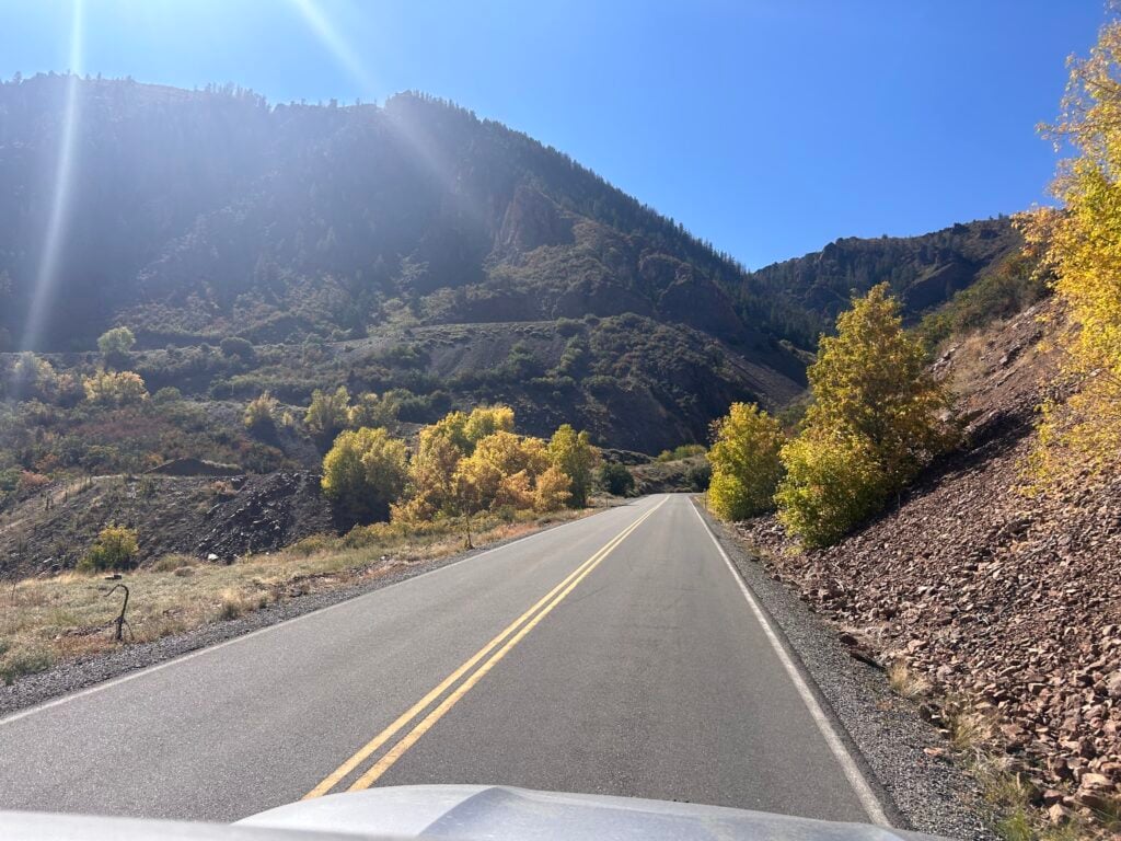 Steep road going up in Colorado. Yellow aspen trees are on the side of the road