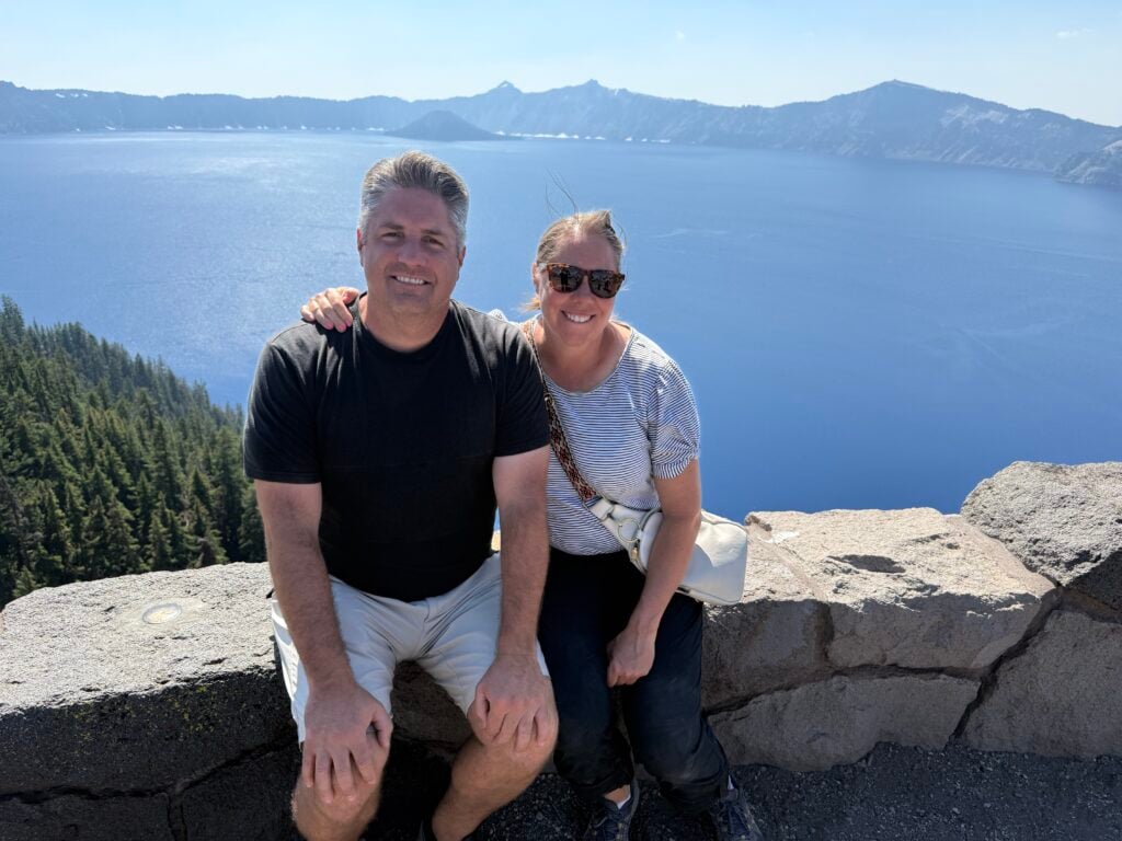 Man and woman sitting on a stone wall with Crater Lake in the backgound