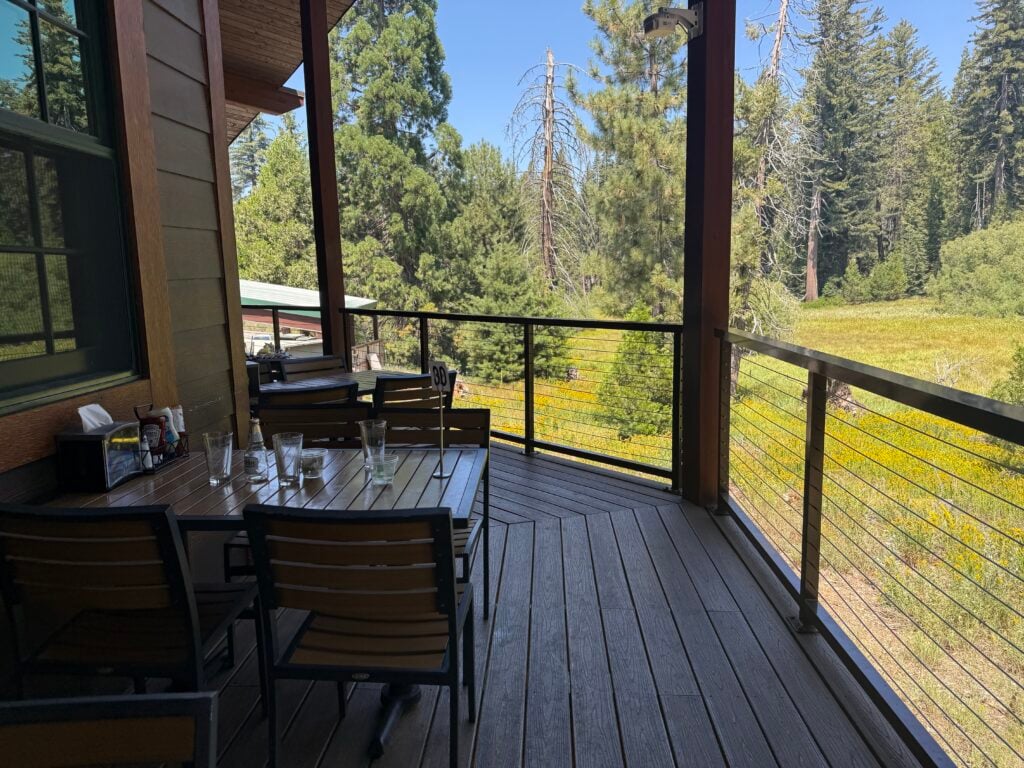 Outdoor seating on a deck in the mountains with views of a green meadow and pine trees