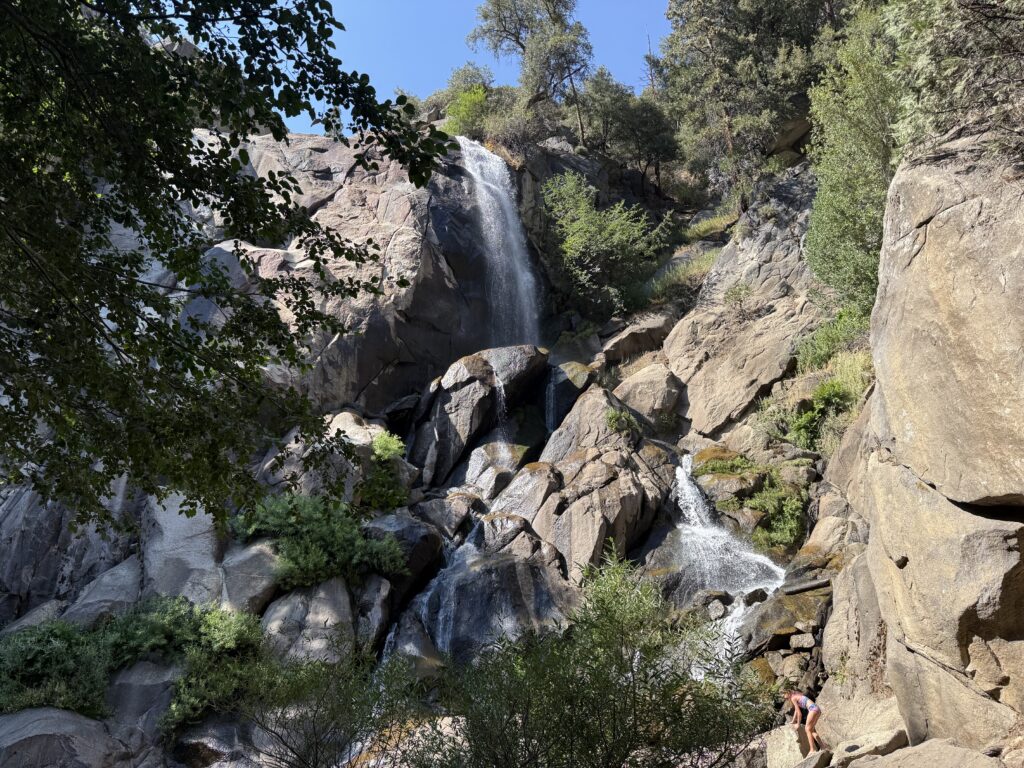 Towering waterfall surrounded by trees and boulders.