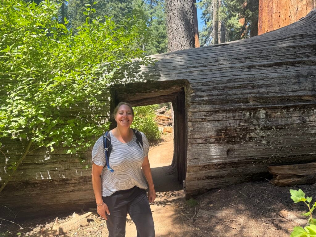 Woman standing in front of a tree that has a tunnel carved into it
