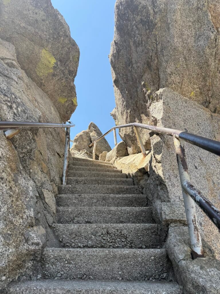 Stone stairs with metal railings going through large granite rocks