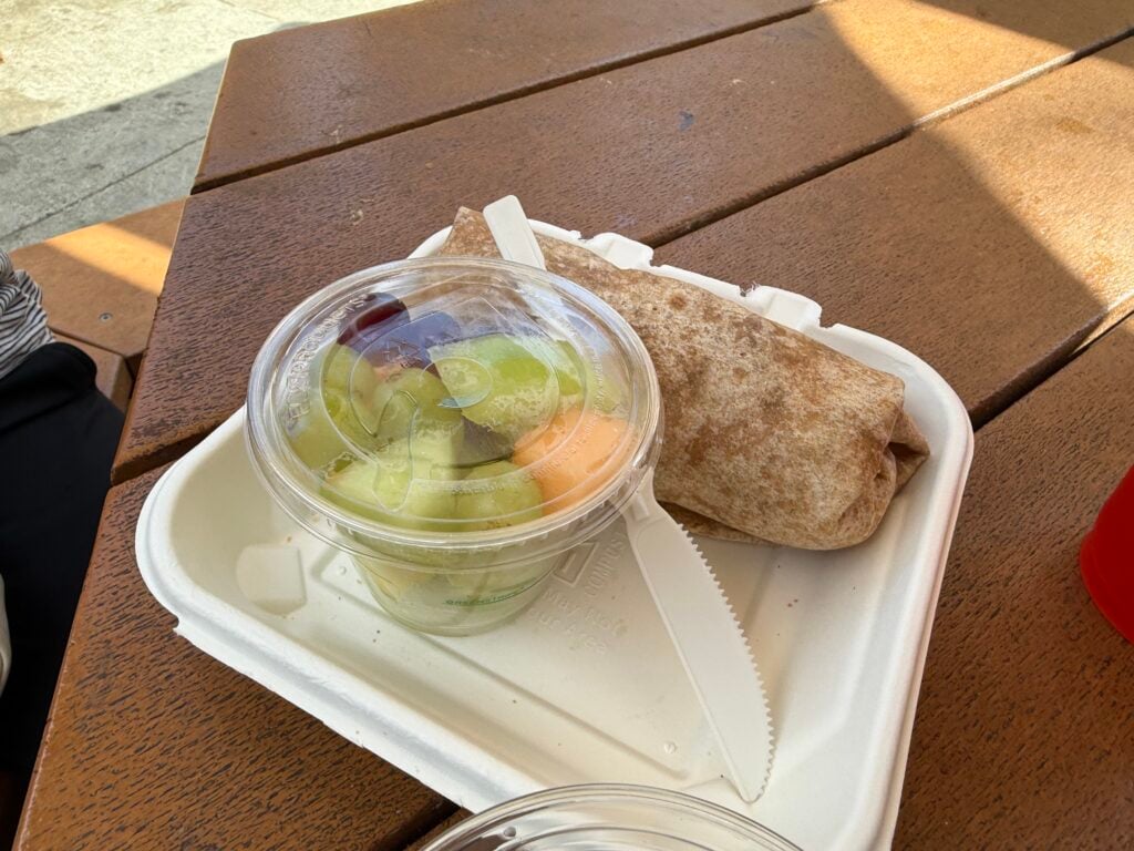Burrito and fruit cup with plastic knife on a table
