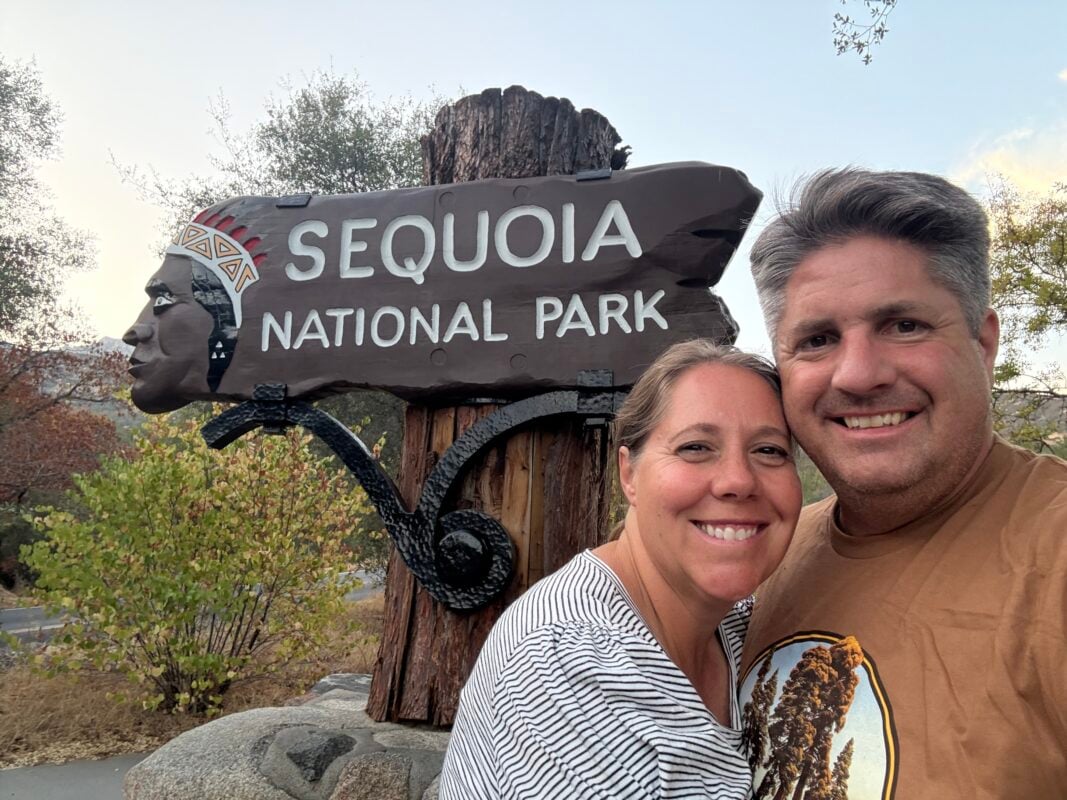 Man and woman infront for sequoia entrance sign. The entrance sign has an indian on it