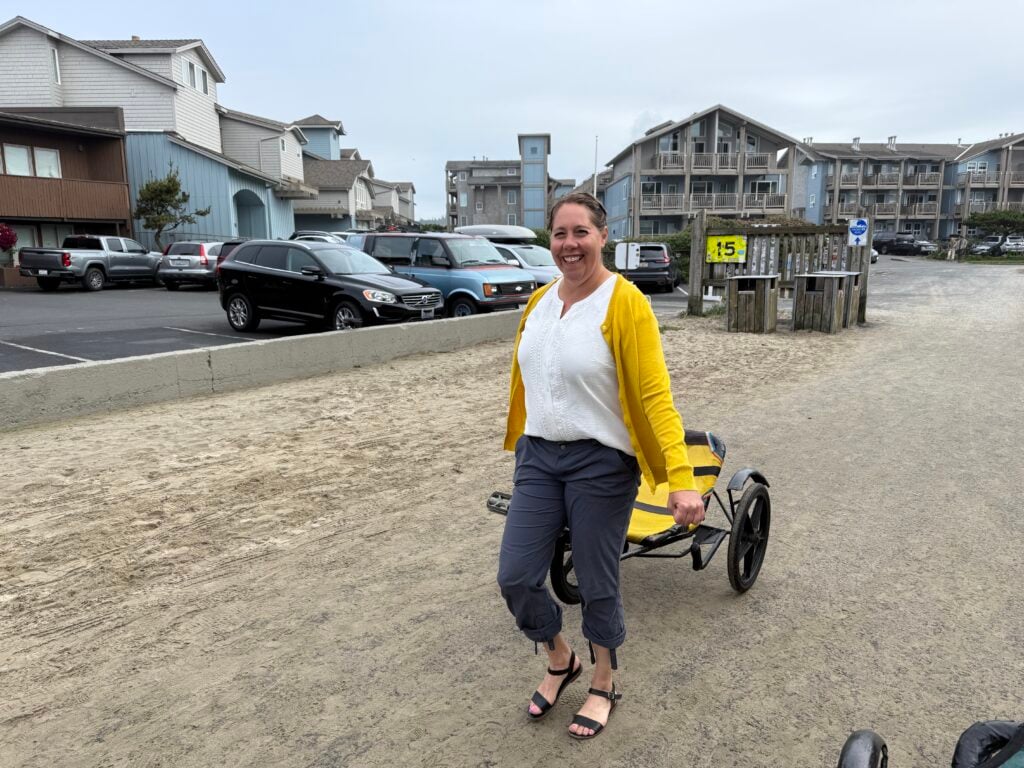 woman pulling recumbent bike along beach near parking lot