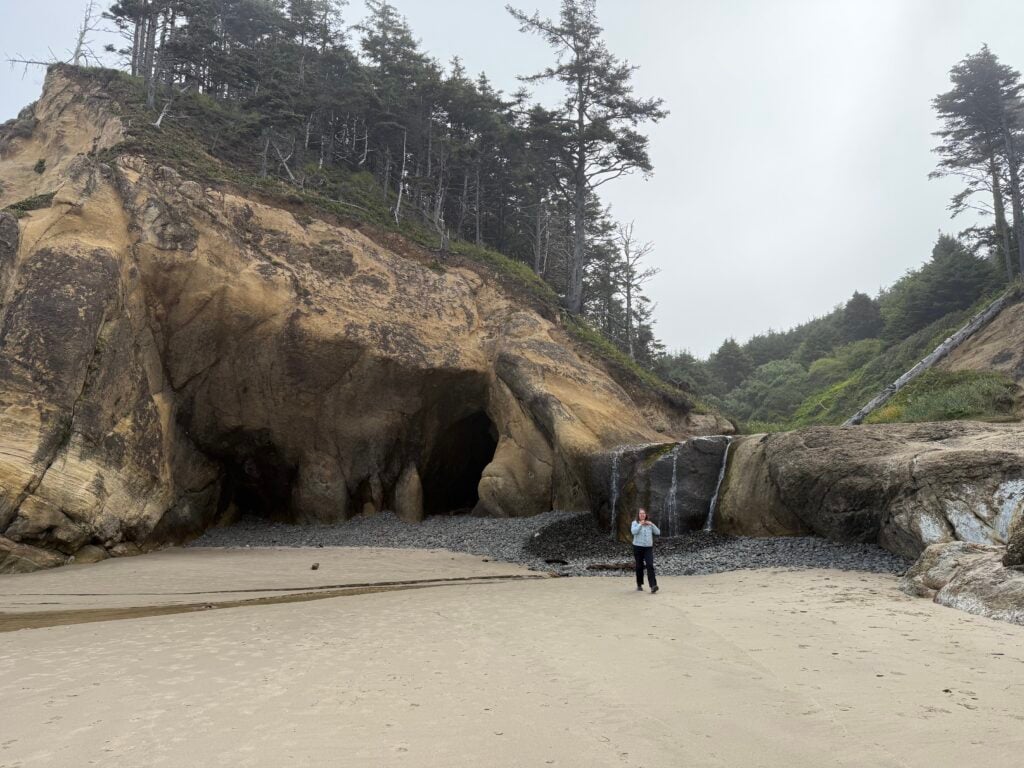 woman standing in front of beach caves and small waterfall