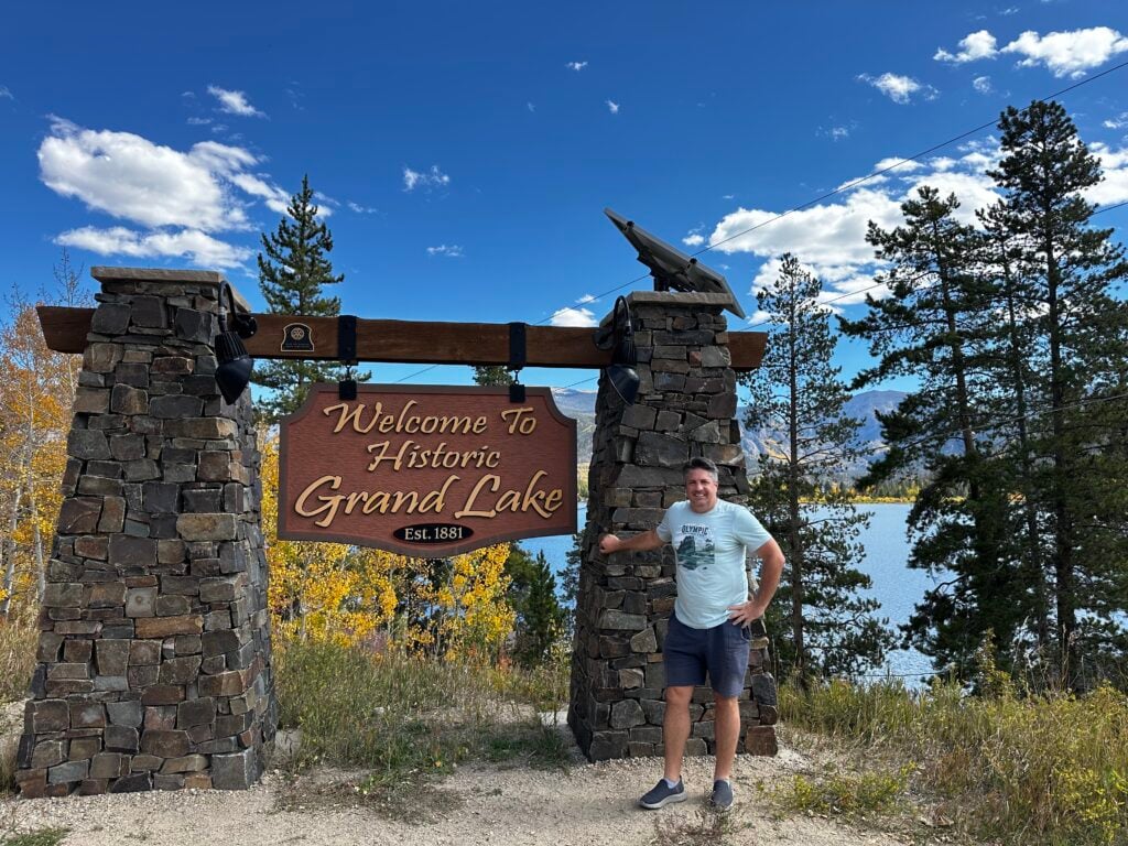 man standing near Grand Lake sign