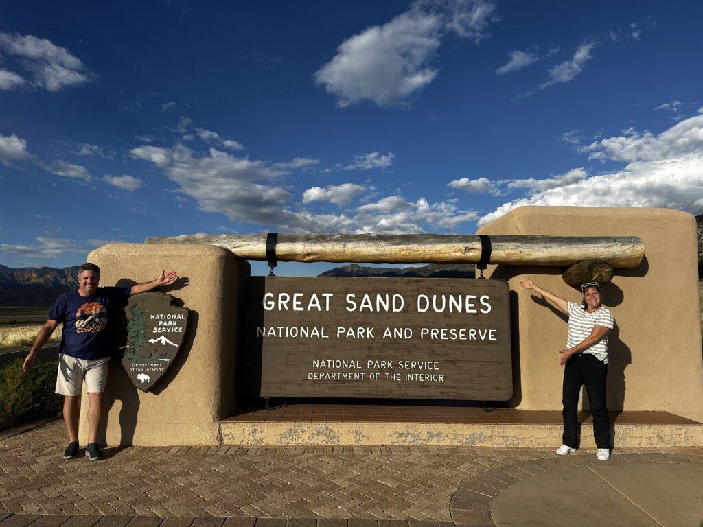 man and woman near Great Sand Dunes sign