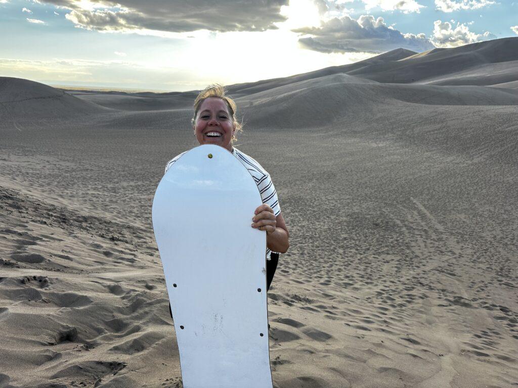 woman holding sandboard in sand dunes