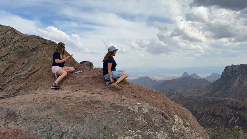 women sitting on cliff looking at view