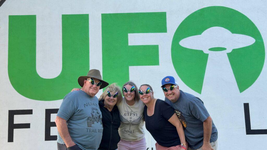 people wearing alien eyes in front of UFO sign