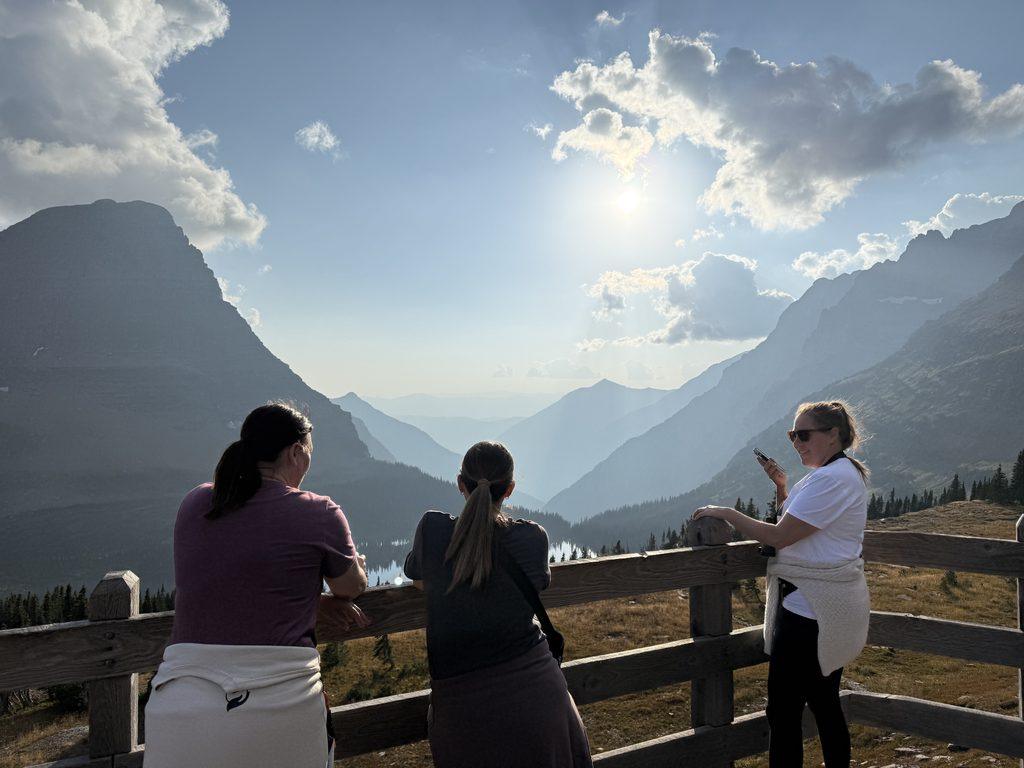 women looking at view behind wooden fence in mountains