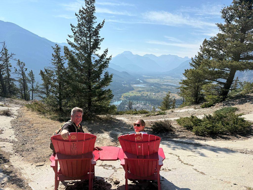 man and woman sitting in red Adirondack chairs overlooking valley