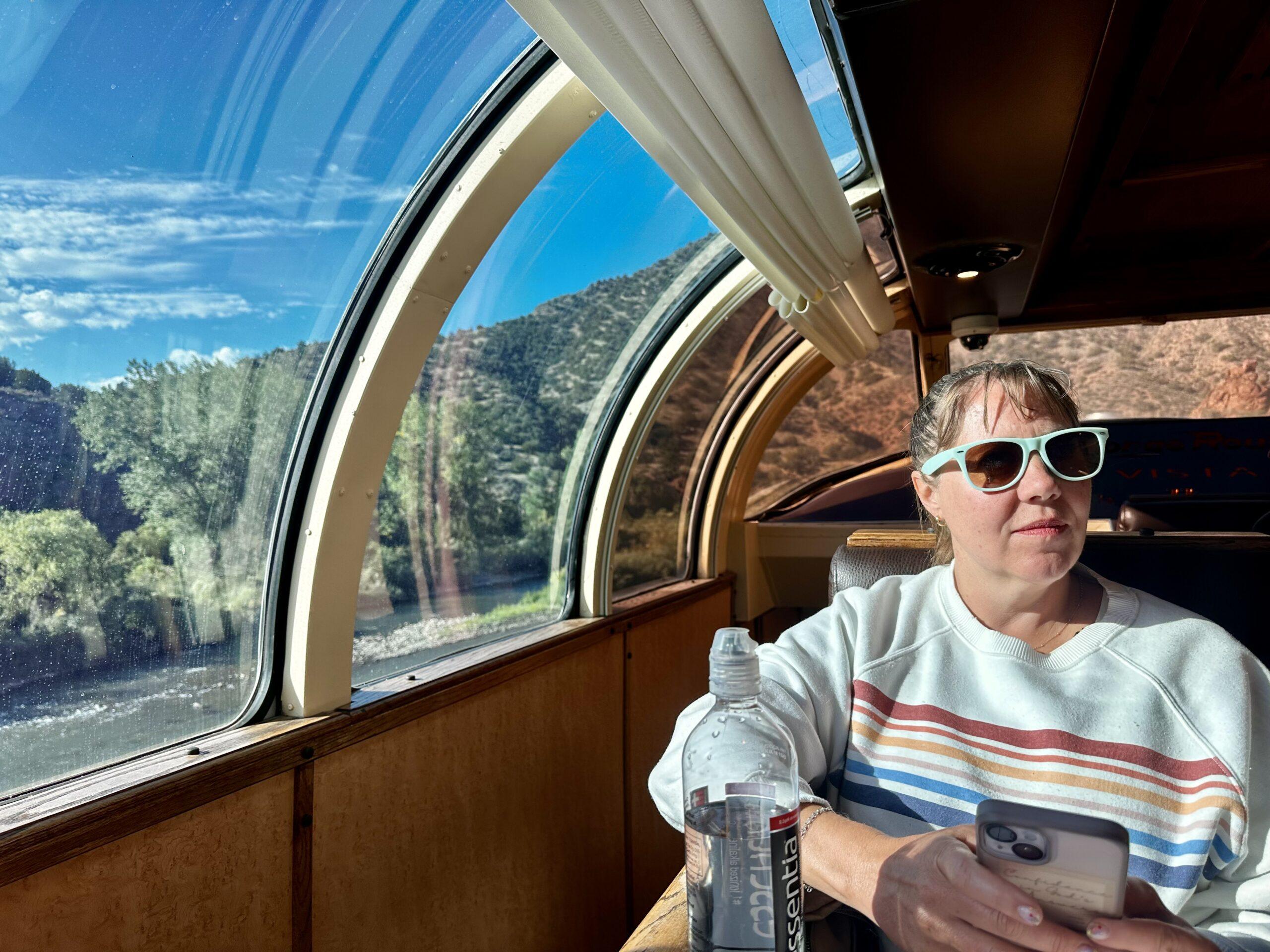 Cheryl seated beside curved Vista Dome windows with the Arkansas River outside