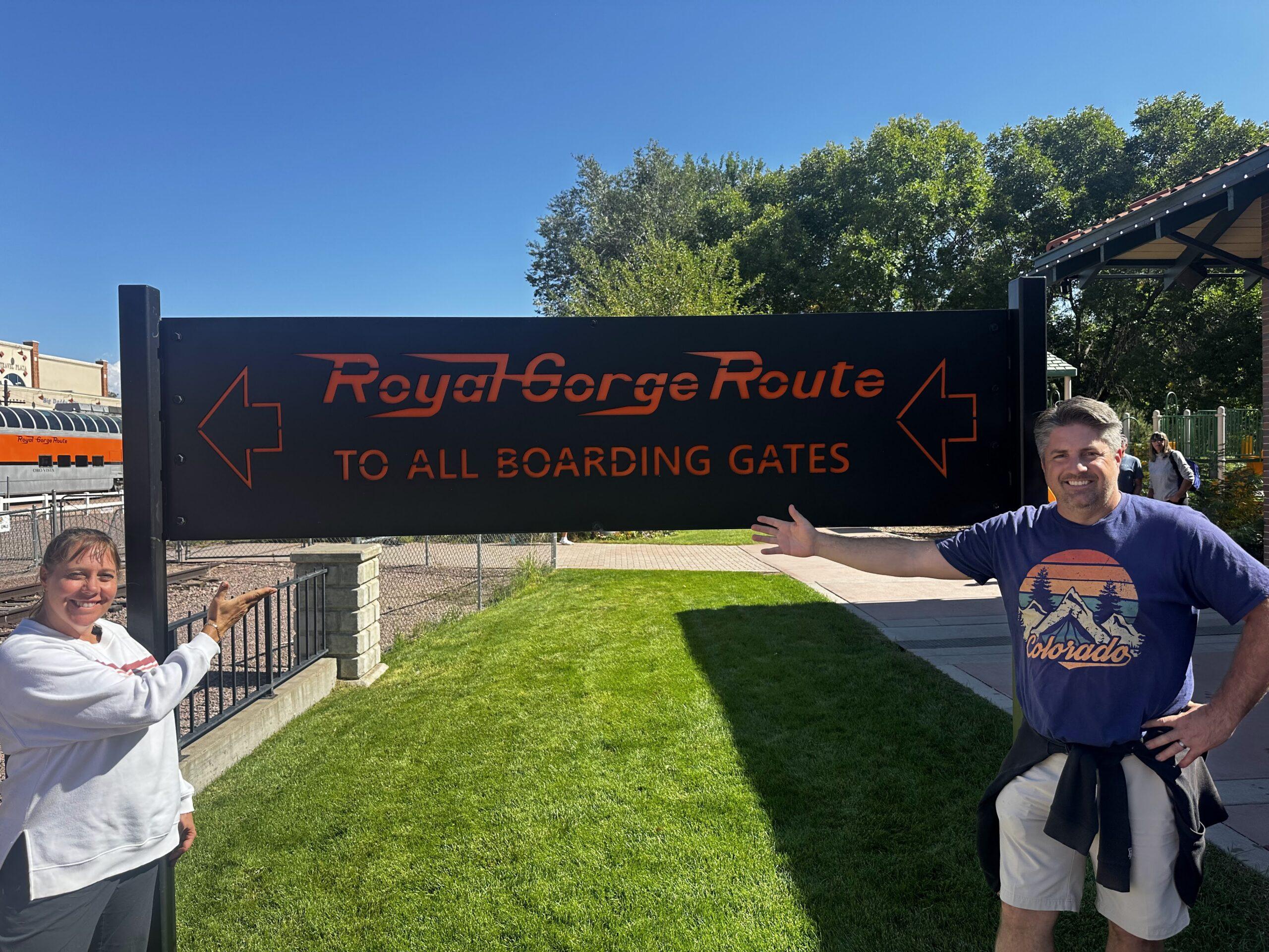 Cheryl and Matt pointing to the Royal Gorge Route boarding gates sign in Cañon City
