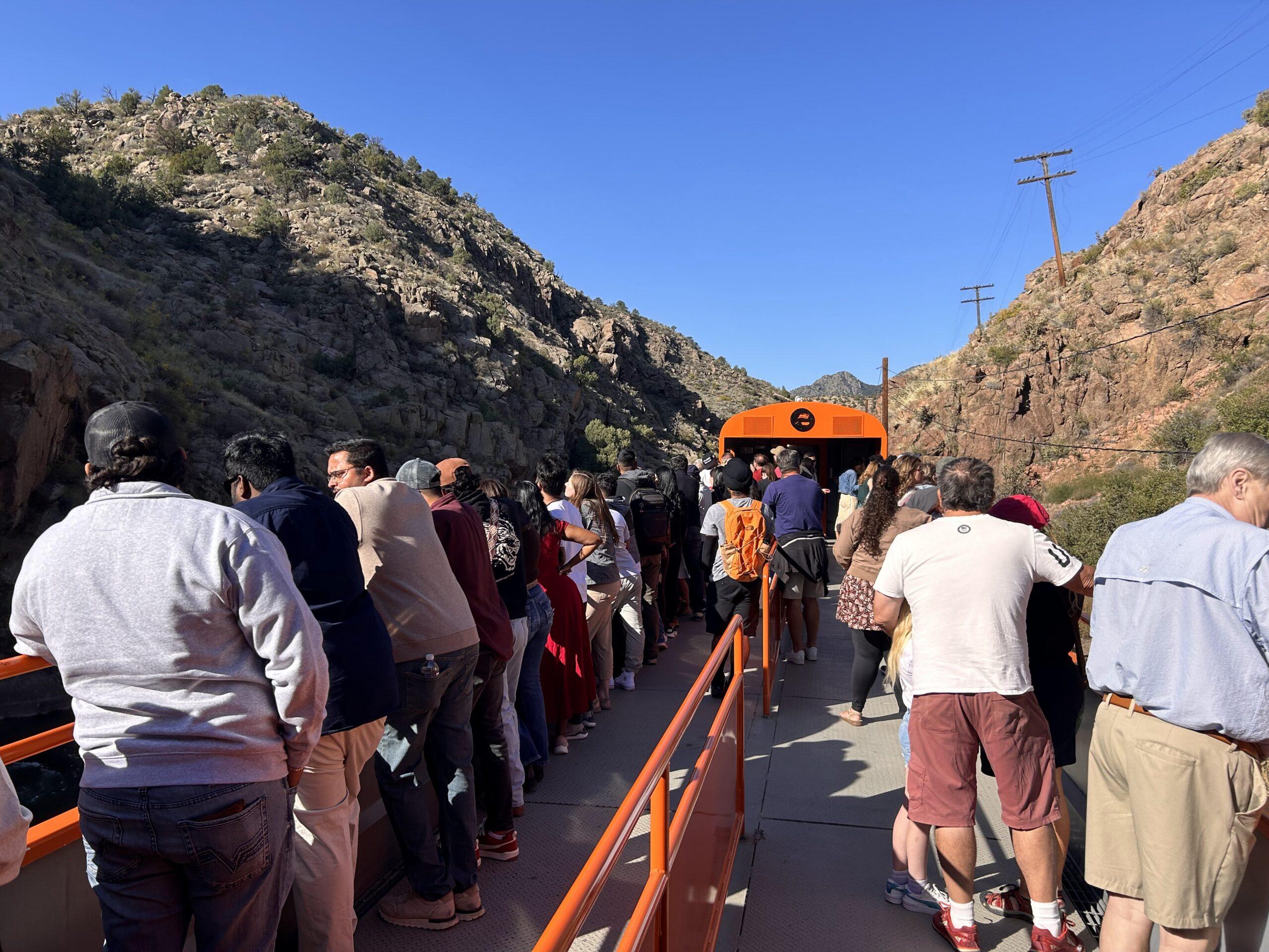 Passengers standing along the railings of a crowded open-air train car in Royal Gorge