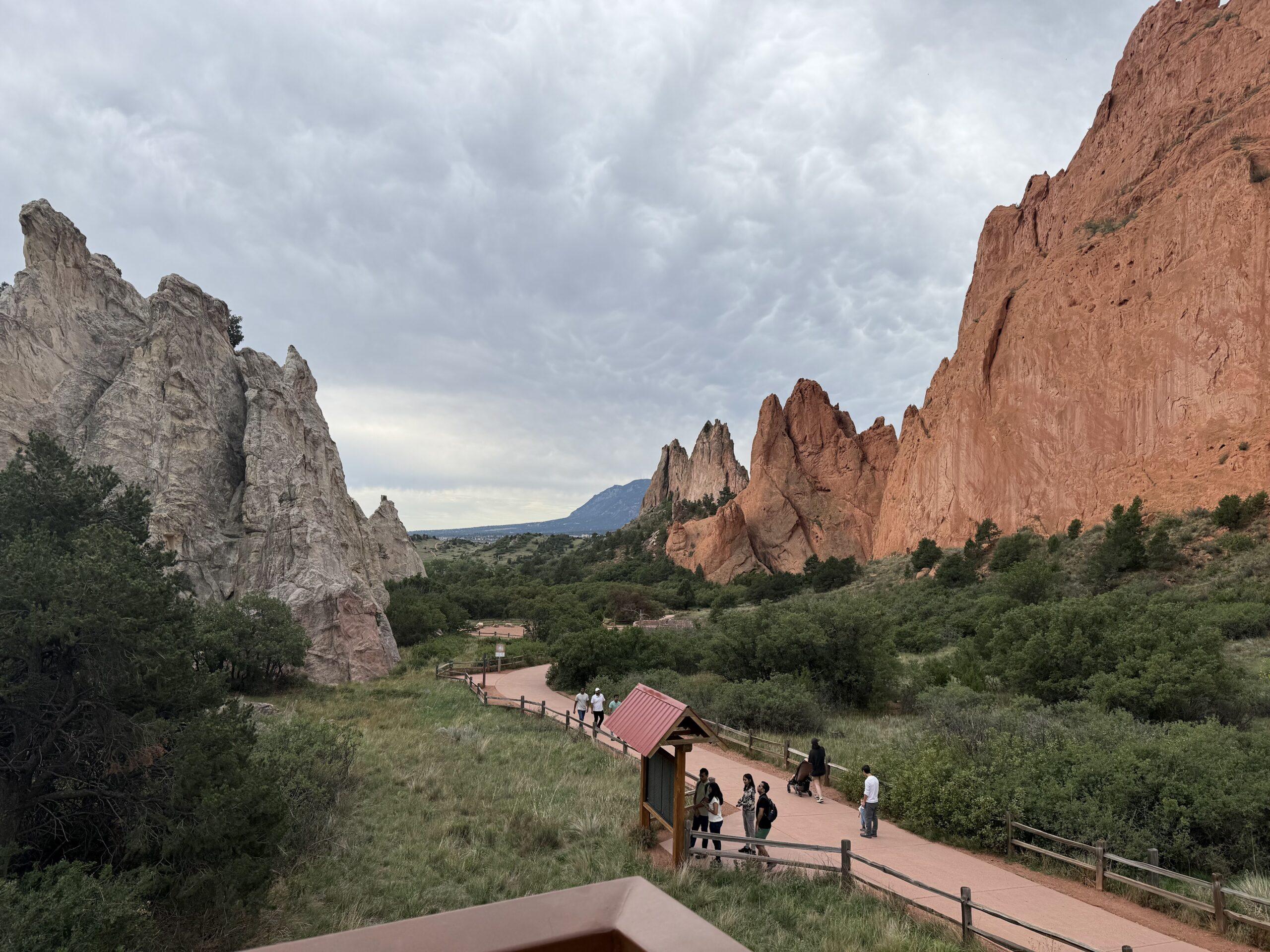 Visitors walking a paved path between red and white rock formations at Garden of the Gods