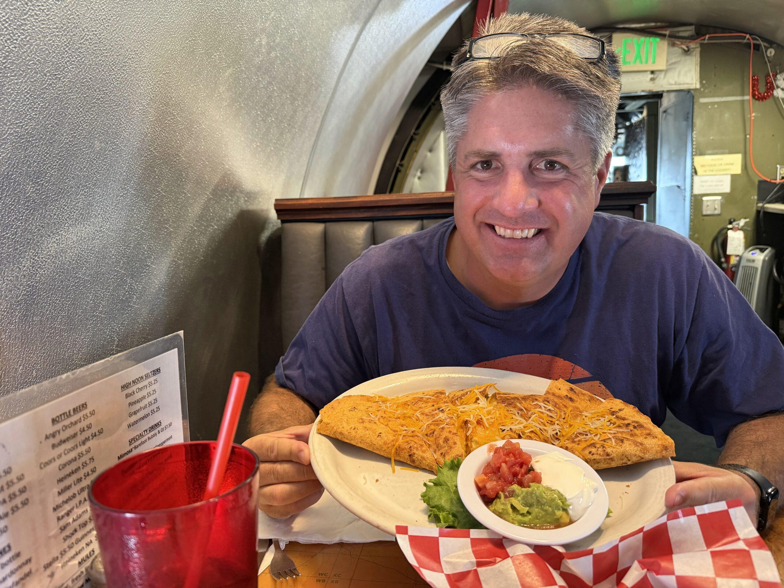 Matt holding a plate of quesadillas while seated inside the airplane at The Airplane Restaurant