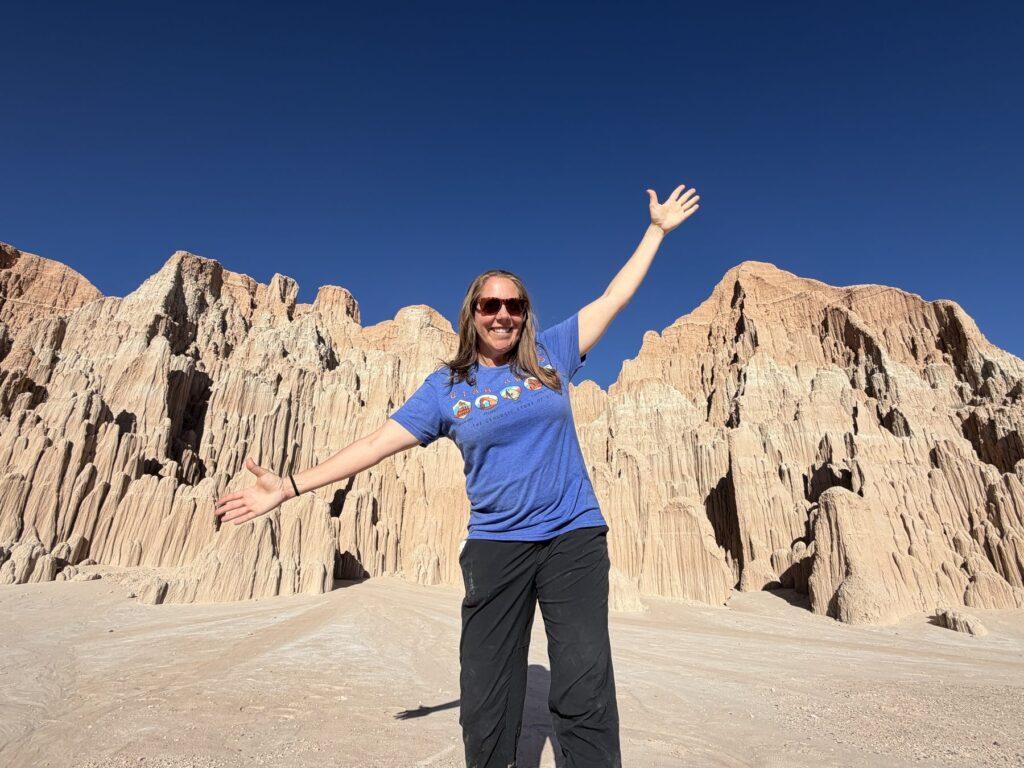 Cheryl smiles with her arms spread in front of the clay formations at Cathedral Gorge State Park.