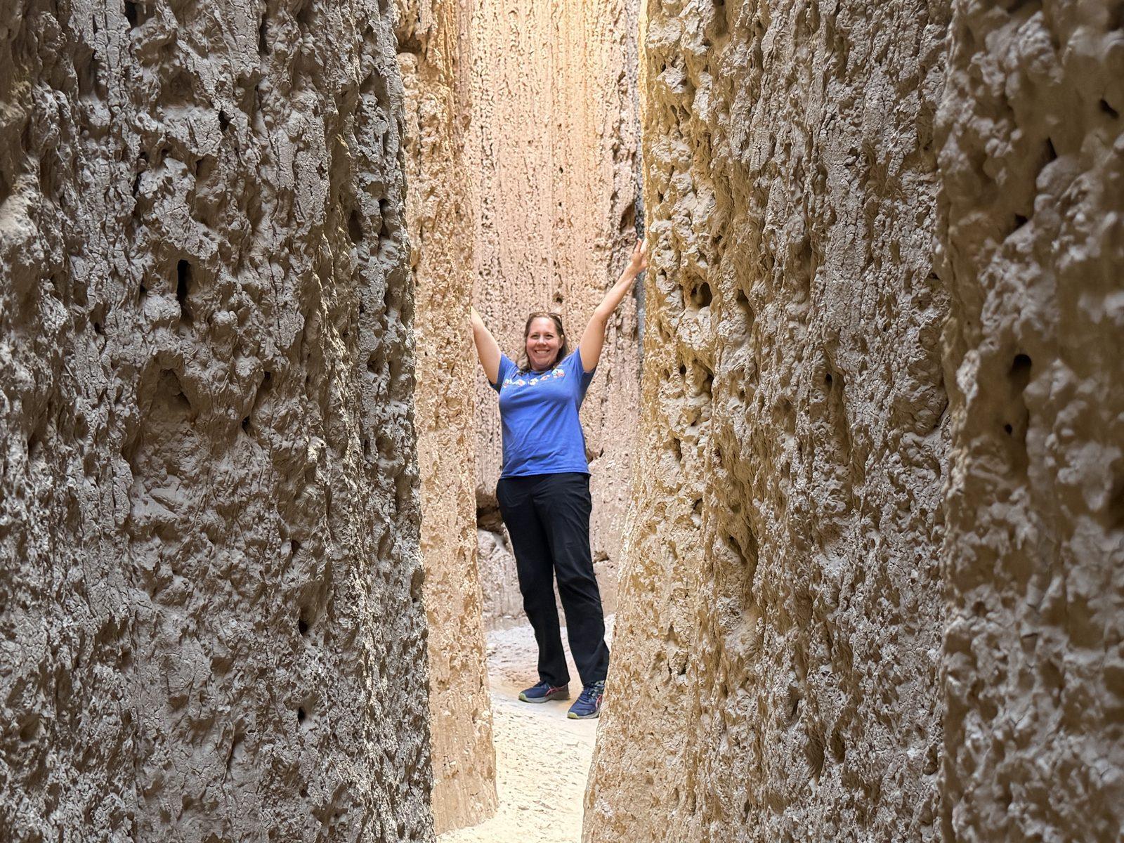 Cheryl raises her arms between the tall, narrow walls of a Cathedral Gorge slot canyon.