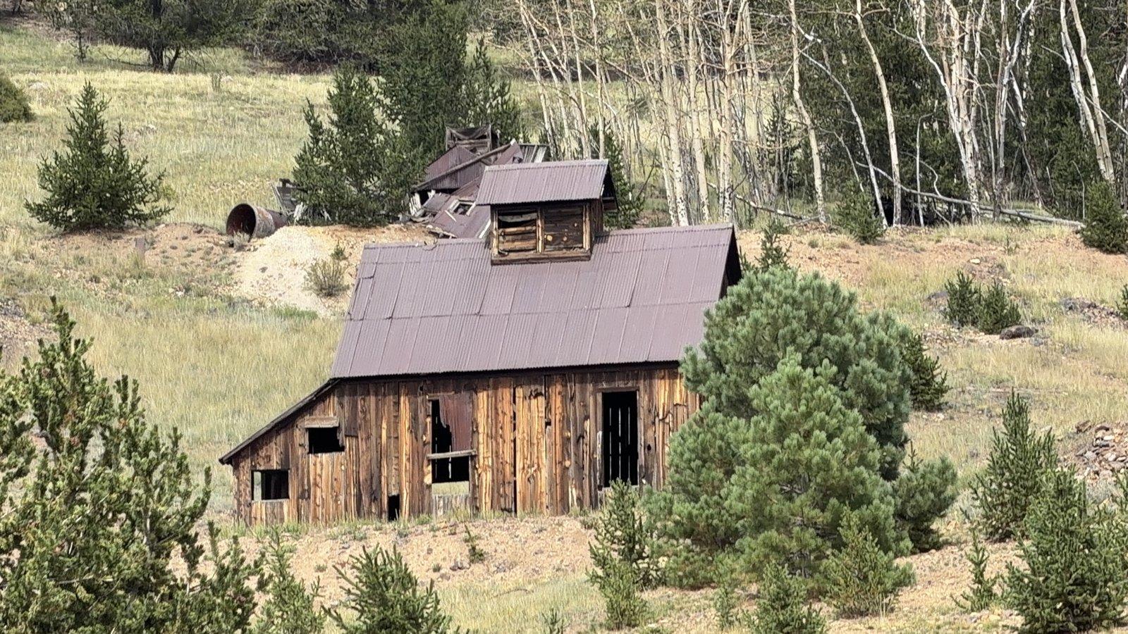 Weathered wooden mining building on a grassy hillside below a grove of aspens near Cripple Creek.
