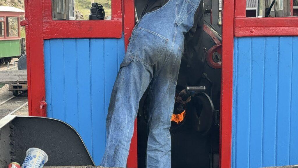 Engineer leaning over the glowing firebox inside the red and blue Cripple Creek steam locomotive.