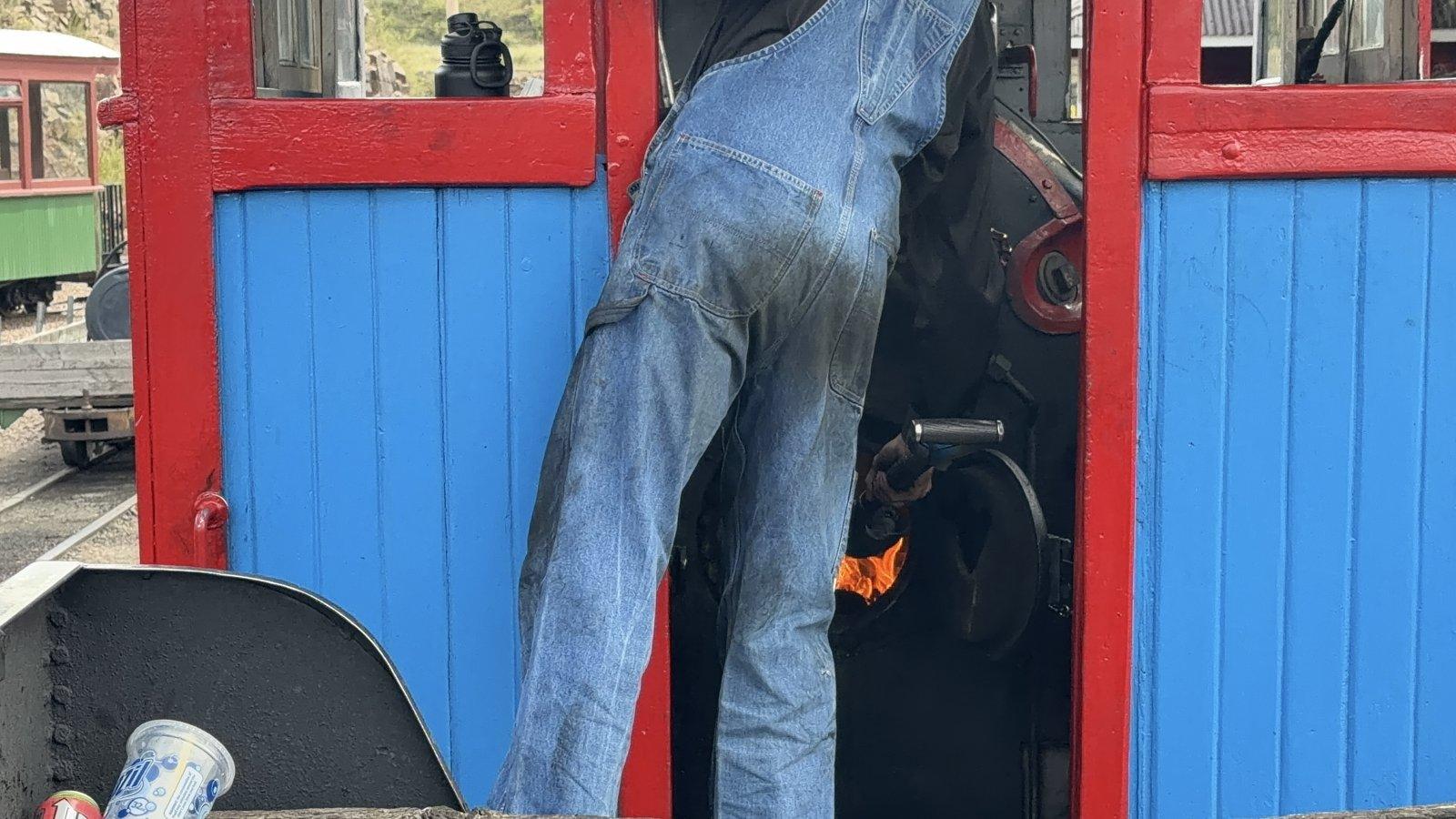 Engineer leaning over the glowing firebox inside the red and blue Cripple Creek steam locomotive.