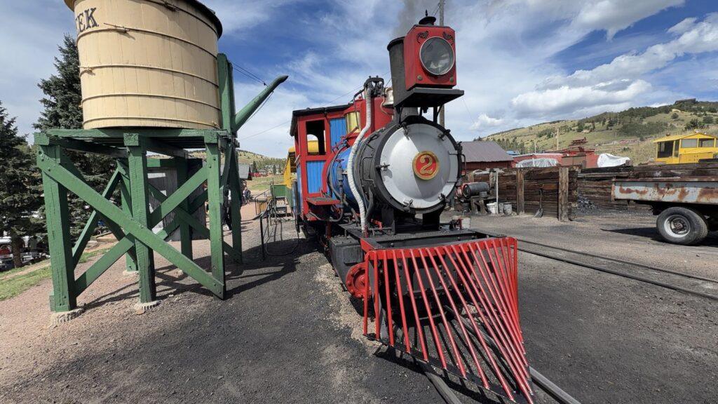 Red and blue No. 2 steam locomotive beside the wooden water tower in Cripple Creek, Colorado.