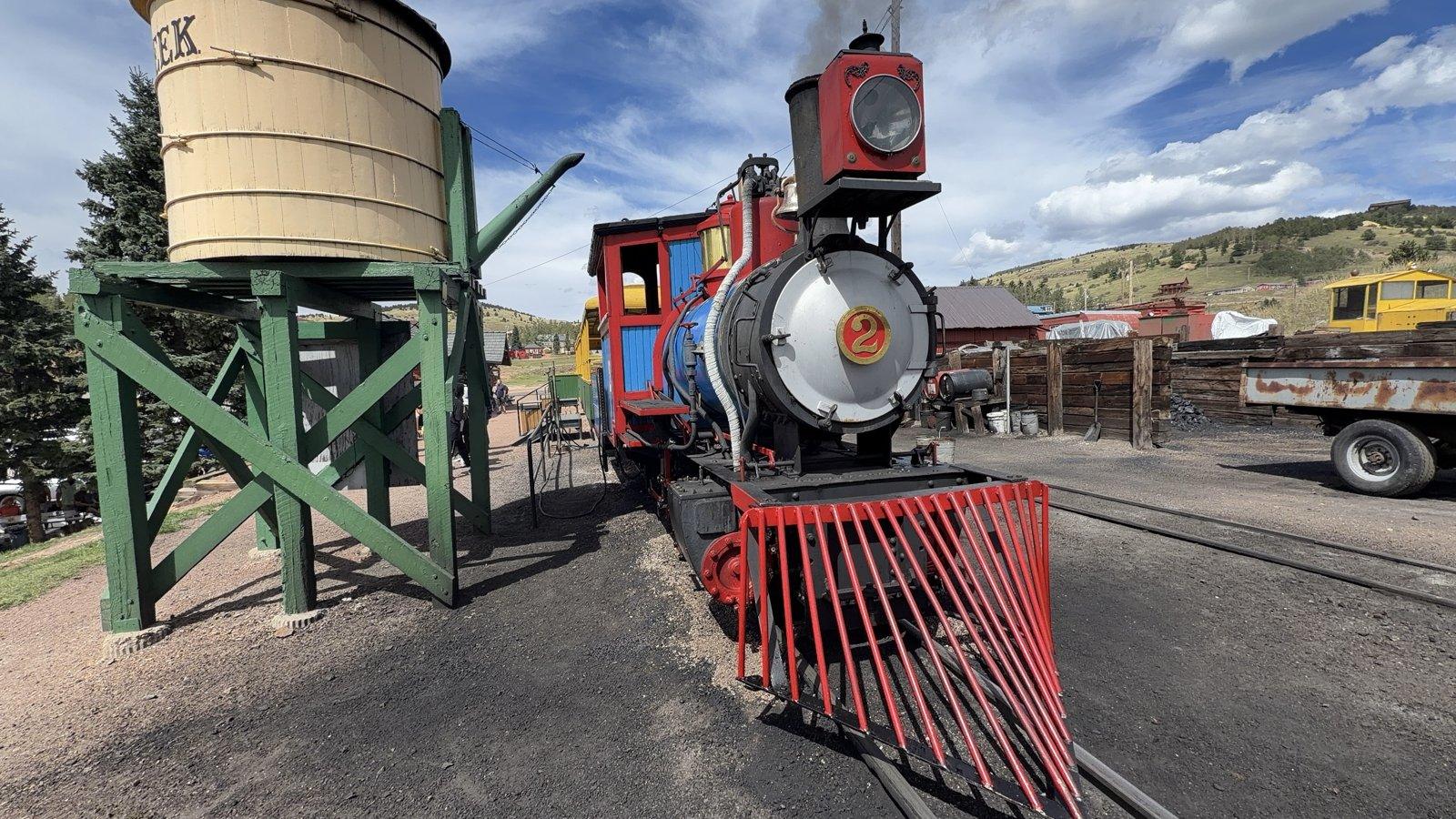Red and blue No. 2 steam locomotive beside the wooden water tower in Cripple Creek, Colorado.