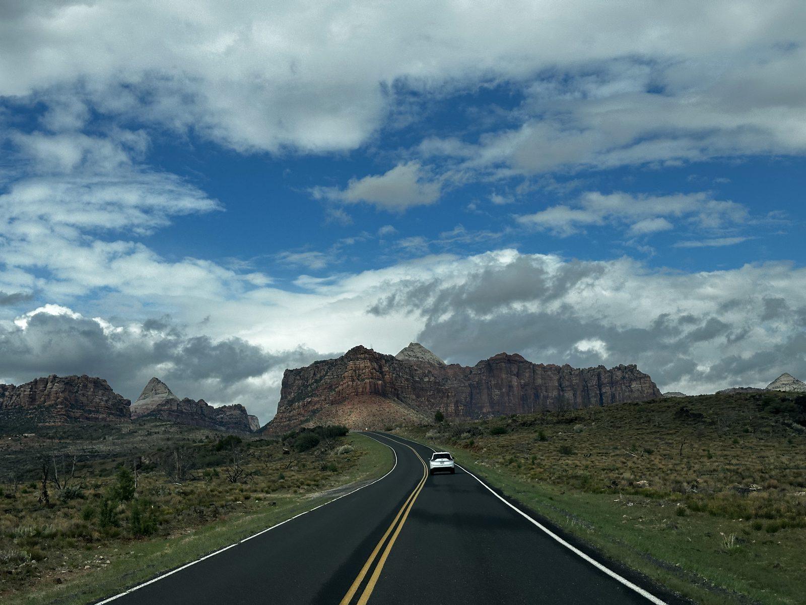 Kolob Terrace Road winds toward sandstone mesas beneath scattered clouds in Zion National Park.